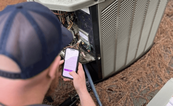 technician referencing Amplinks mobile app while inspecting an outdoor condenser unit.